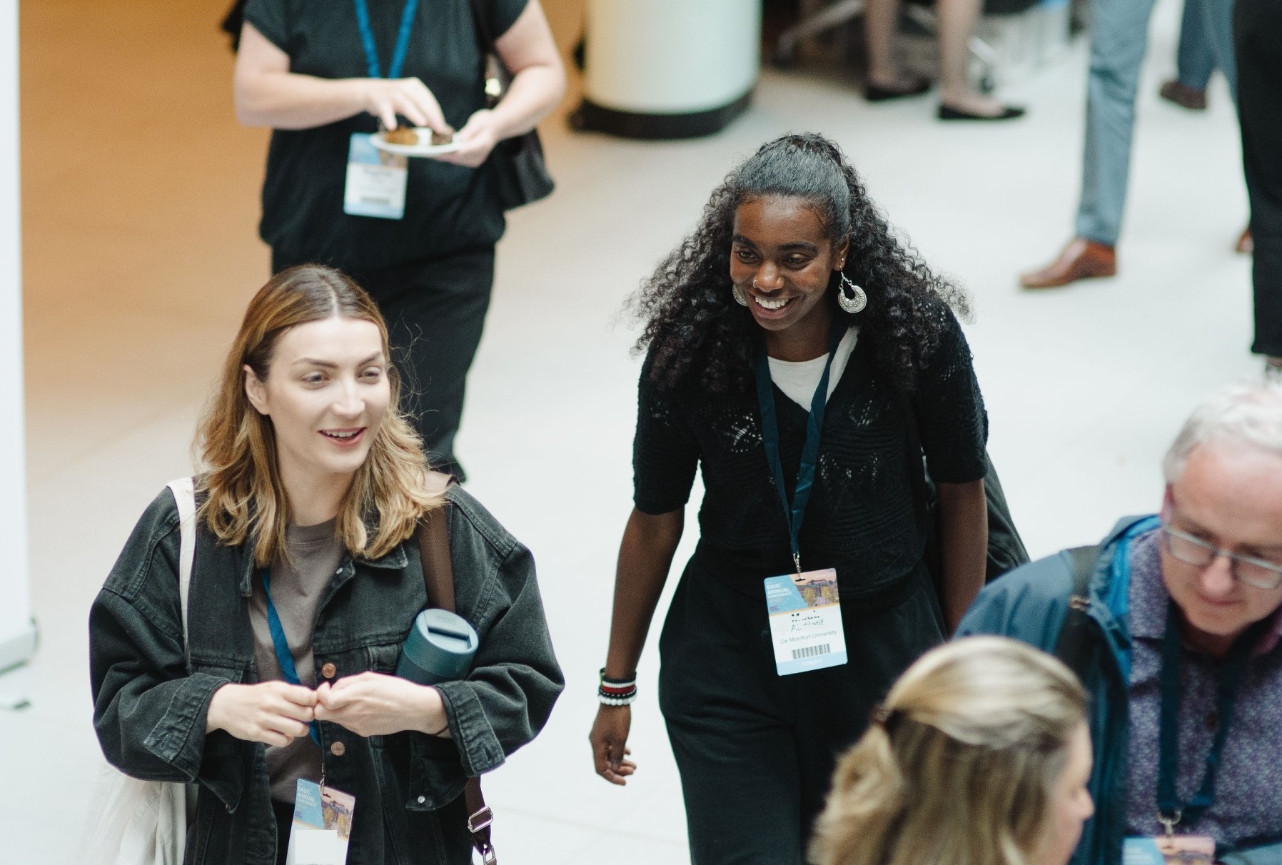 A man wearing a lanyard and a flowery shirt stands in front of a large lush green fern trees.